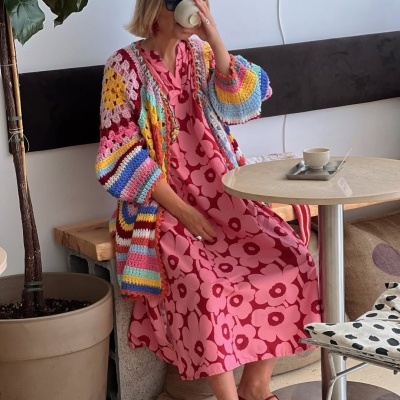 Mulher com veste de croché colorida e vestido rosa com flores sentada numa cafeteria