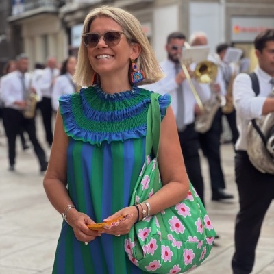 Mulher com vestido azul e verde e bolsa verde com flores numa rua urbana