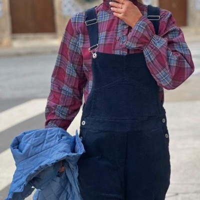 Pessoa com camisa xadrez vermelha e azul e jardineira preta segurando casaco azul acolchoado