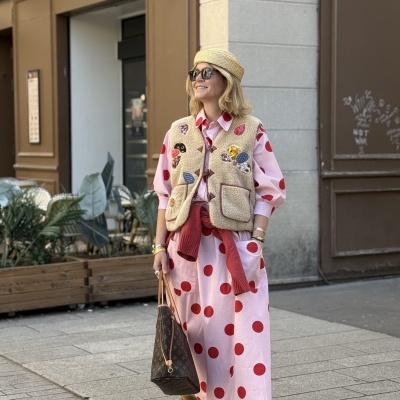 Mulher com vestido rosa e bolinhas vermelhas, colete de pelo bege e chapéu de palha