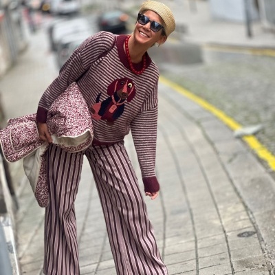 Mulher sorridente com suéter estampado de cão, calças largas às riscas e chapéu de palha na rua