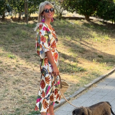 Mulher com vestido estampado e sapatos rosas a passear cão castanho na rua