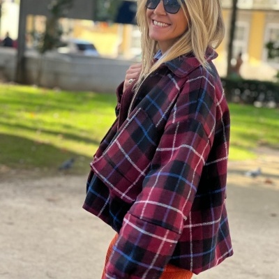 Mulher a usar casaco xadrez vermelho e preto com óculos de sol num parque.