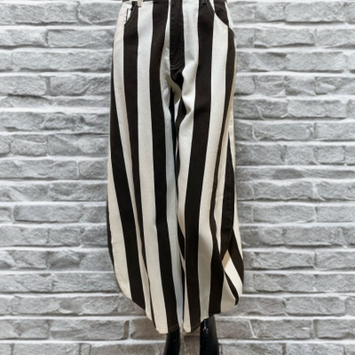 Calças largas com riscas verticais a preto e branco num manequim frente a uma parede de tijolos branca.