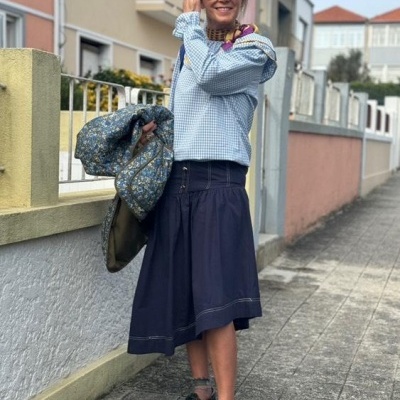Mulher com camisa azul clara e saia azul escura numa rua urbana