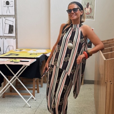 Mulher com vestido comprido listrado e sandálias pretas em espaço interior com paredes claras e arte na parede