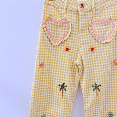 Calças amarelas com padrão xadrez branco e bordados tropicais suspensas em cabide