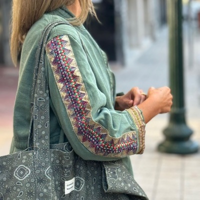 Casaco verde com bordados multicoloridos e saco de tecido cinzento com padrão branco em ambiente urbano