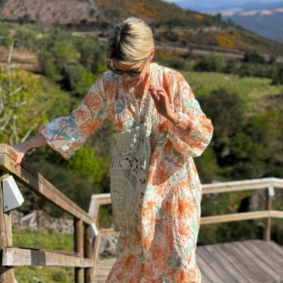 Vestido longo floral em tons de laranja, branco e verde, tecido leve, mulher em escadaria de madeira ao ar livre