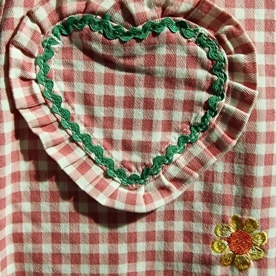 Detalhe de tecido xadrez vermelho e branco com bolso em forma de coração e bordados florais.