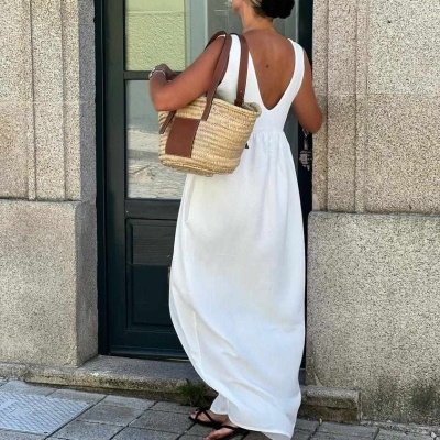 Mulher de vestido branco, carteira de palha e cabelo preso, junto a porta exterior