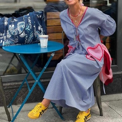 Mulher com vestido xadrez azul e branco, ténis amarelos e mochila azul sentada ao lado de mesa azul