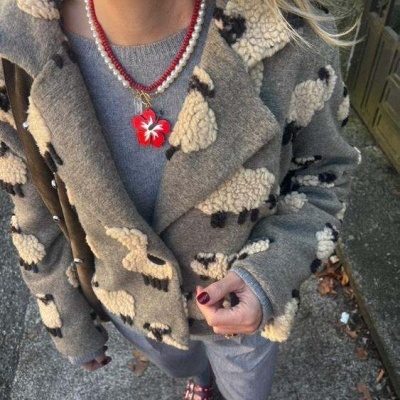 Mulher a usar casaco cinzento com padrão ovelha, colar com pendente vermelho, calças cinzentas e sapatos vermelhos