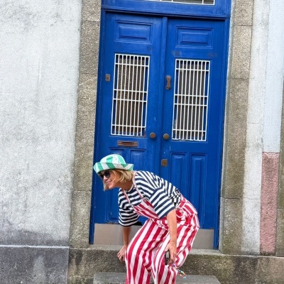 Pessoa loira com roupa colorida e chapéu junto a porta azul