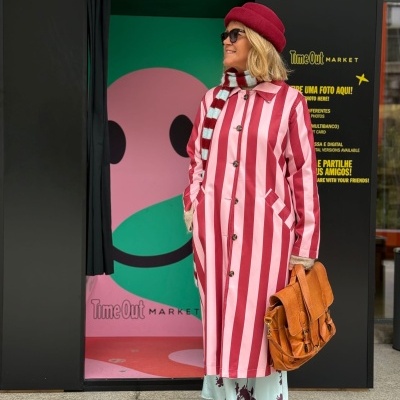Mulher com gabardina rosa e vermelha às riscas em frente a cabine fotográfica