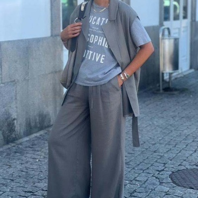 Mulher com conjunto cinza, t-shirt com texto branco, calças largas e sapatilhas brancas