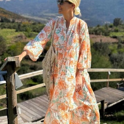 Vestido comprido floral laranja e verde com manga comprida, mulher de óculos ao ar livre.
