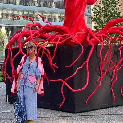 Mulher vestida em frente a escultura vermelha de árvore com raízes 