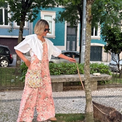 Mulher a passear com cachorro em rua com macacão rosa floral, casaco branco e saco de pano colorido