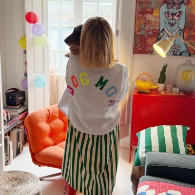 Mulher de costas com camisola cinza e saia às riscas numa sala colorida