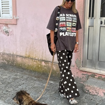 Mulher com t-shirt cinzenta escura estampada e calças pretas com bolinhas brancas a passear cão.
