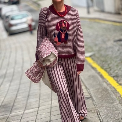 Mulher com camisola riscada e calças largas riscas com cão bordado e óculos escuros a andar na rua