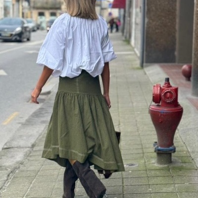 Mulher com blusa branca, saia verde e botas pretas na calçada de rua