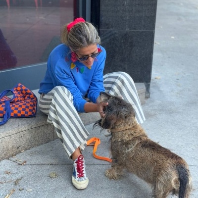 Pessoa sentada a acariciar um cão num ambiente urbano com bolsa azul e laranja ao lado