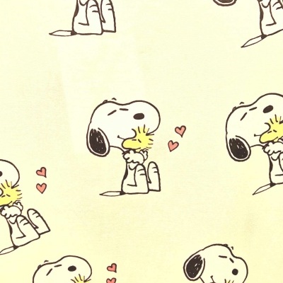 Pano amarelo claro com padrão de Snoopy a abraçar Woodstock e corações cor-de-rosa