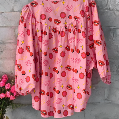 Camisa rosa com padrão colorido pendurada em cabide preto contra parede de pedra cinzenta