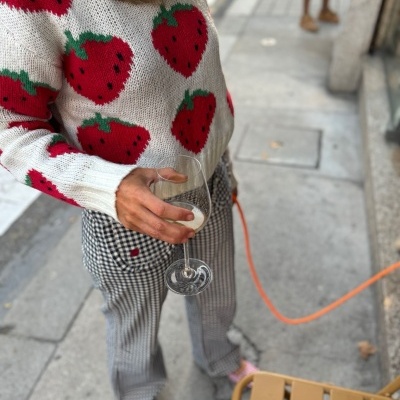 Pessoa com suéter de morangos, calças xadrez e sapatos rosa segurando taça numa calçada