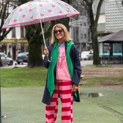 Pessoa com casaco azul e suéter rosa segurando guarda-chuva transparente com corações