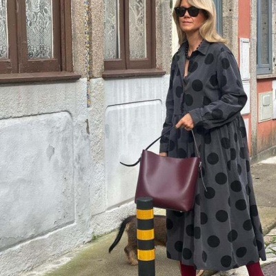 Mulher com vestido longo cinza de bolinhas pretas, meias vinho, sapatos pretos e óculos escuros