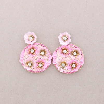 Brincos pink com flores bordadas e detalhes em pérola sobre fundo cinzento