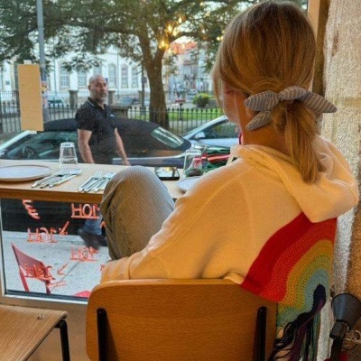 Casaco branco com padrão de arco-íris colorido nas costas, pessoa sentada numa cadeira de madeira