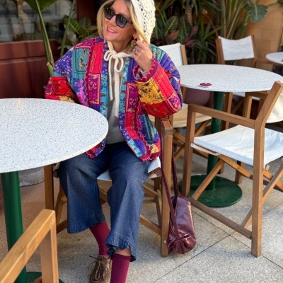 Mulher sentada com casaco colorido e gorro branco num café ao ar livre