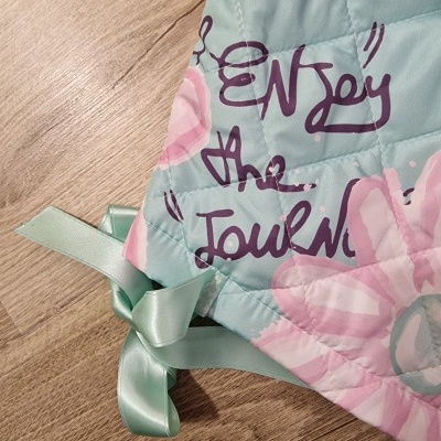 Tapete acolchoado verde menta com flores rosas, laço verde e texto roxo 