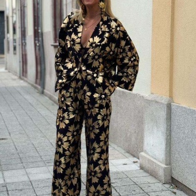 Mulher com macacão preto com flores douradas e sapatos dourados numa rua