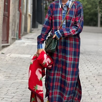 Mulher com vestido xadrez azul e vermelho, casaco vermelho com rosa, sapatos coloridos e óculos escuros numa rua