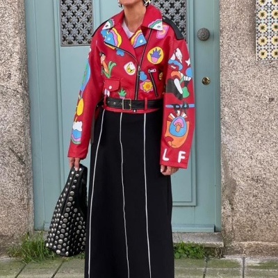 Mulher com casaco vermelho estampado, saia preta com riscas brancas, bolsa preta com tachas e óculos escuros