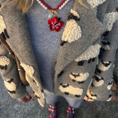 Casaco cinzento com padrão de ovelhas, colar com flor vermelha, calças cinzentas e sapatos vermelhos