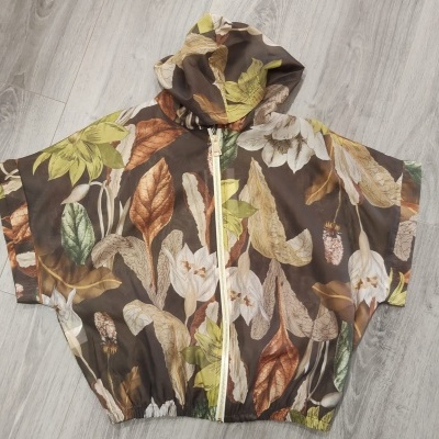 Casaco com capuz e padrão floral colorido em tons de castanho, verde e amarelo, com fecho creme.