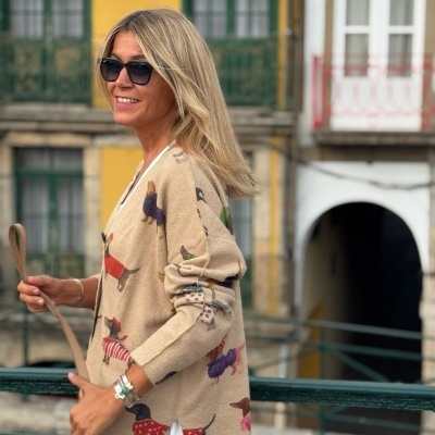 Camisola bege com padrões coloridos de cães e mulher com óculos escuros num ambiente urbano