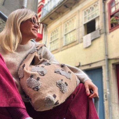 Mulher sentada com mala bege de tecido com padrões cinza em relevo