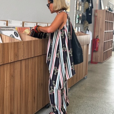 Mulher com vestido às riscas listradas e padrão de cactos a olhar para discos vinil num expositor de madeira.