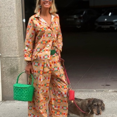 Mulher com pijama estampado e sapatos laranja com cão na trela numa rua