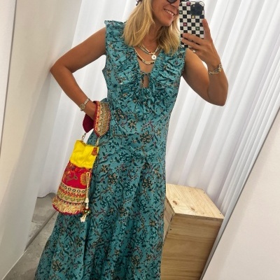 Mulher com vestido azul floral, azul, bolsa colorida, chapéu castanho e óculos escuros na frente de espelho