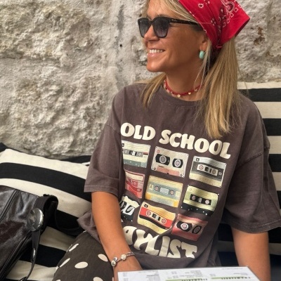 Mulher com t-shirt estampada de cassetes, lenço vermelho e óculos de sol sentada com menu à frente