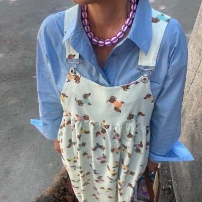 Vestido de alças com padrão de cães dachshund coloridos usado com camisa azul clara e colar roxo e branco