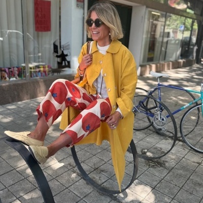 Mulher com casaco amarelo e calças estampadas sentada ao ar livre junto a uma bicicleta